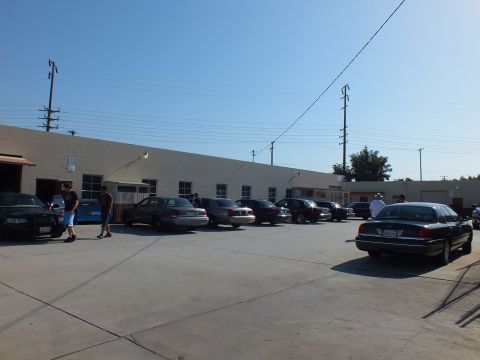 2003 Ford Crown Victoria - Several Panther-platform sedans lined up outside a cinder block shop under clear sky