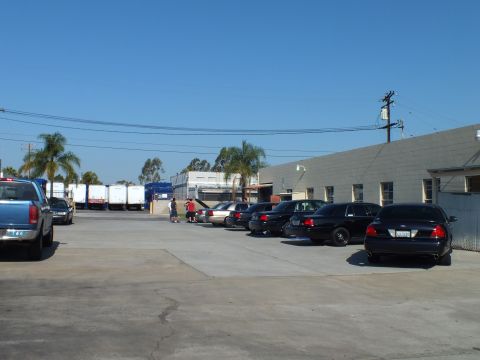 2003 Ford Crown Victoria - Row of dark full-size sedans at a meet, freight containers and palms in background