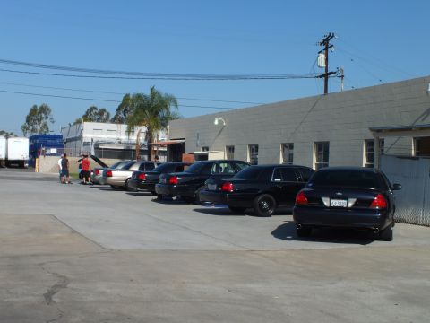 2003 Ford Crown Victoria - Black Panther-platform sedans angled along a block building, plate 7L0939 on near car