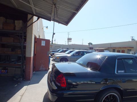 2003 Ford Crown Victoria - Black sedan with tinted windows and spoiler parked at a shop, supplies stored inside bay