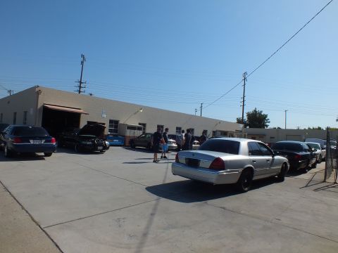 2003 Ford Crown Victoria - Silver Grand Marquis foreground with sedans and people near open garage bays