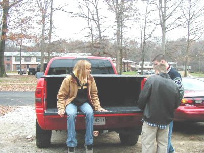 1997 Ford Taurus - A group of people are gathered around the back of a red pickup truck on a cloudy day.