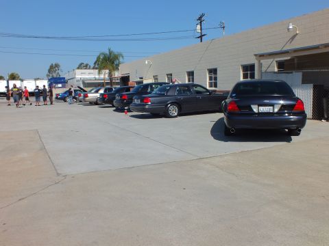 2003 Ford Crown Victoria - Row of dark gray and black sedans at a shop meet, plate visible on near car
