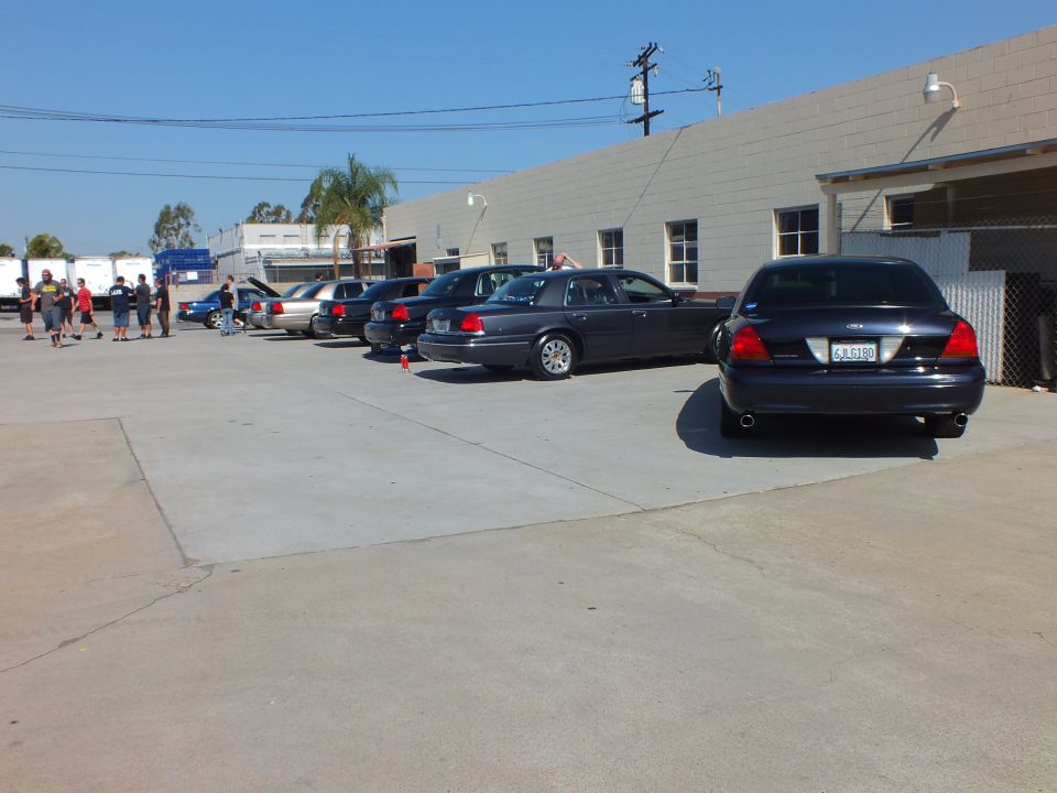 Dark Ford sedans parked along block building with people at far end of lot