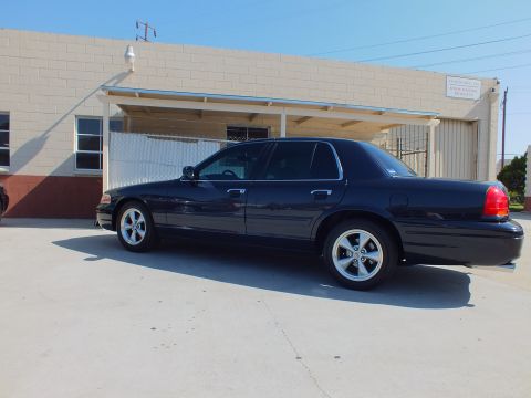 2003 Ford Crown Victoria - Dark blue Crown Victoria parked beside a chain-link fence and beige shop building