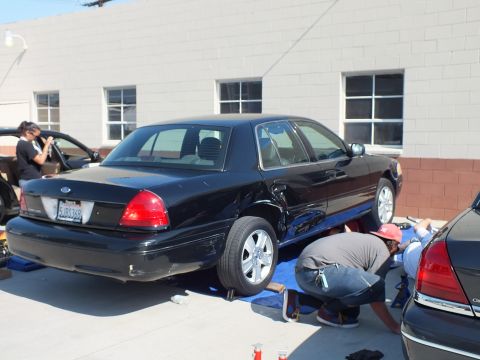 2003 Ford Crown Victoria - Black Crown Victoria plate 5LBE3X9, one person kneeling at side, another with camera