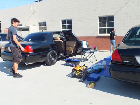 2003 Ford Crown Victoria - Black Crown Victoria LX doors open, snacks and water crates laid on the lot, man standing by