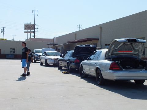 2003 Ford Crown Victoria - Sedans with trunks open lined up, ASCO Metals sign behind, person walking past
