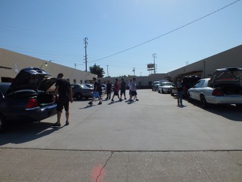 2003 Ford Crown Victoria - Attendees crossing the lot among Panther sedans with trunks open, bright midday sun