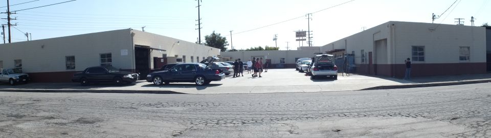 Distant wide view of car meet sedans parked along industrial buildings
