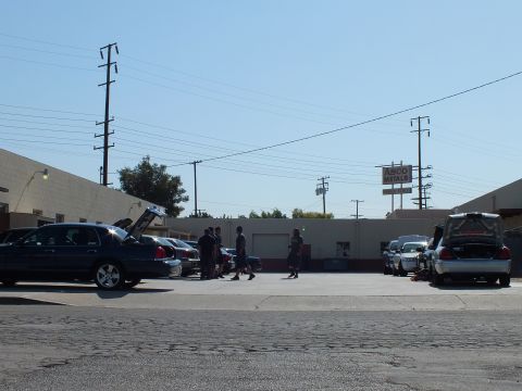 2003 Ford Crown Victoria - Group of attendees and full-size sedans, hoods and trunks open, beside an industrial warehouse.