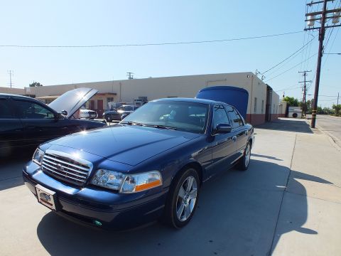 2003 Ford Crown Victoria - Blue Crown Victoria sedan with raised hood and trunk parked on concrete near power lines.