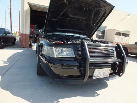 2003 Ford Crown Victoria - Black Crown Victoria with chrome brush guard and raised hood showing engine bay at a garage.