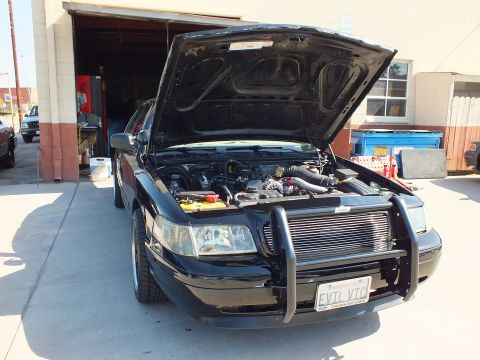 2003 Ford Crown Victoria - Front of a black Ford sedan, hood up exposing the V8 engine and intake, brush guard fitted.