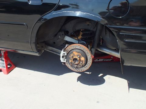 2003 Ford Crown Victoria - Close view of a cross-drilled rear brake rotor and hub on a black car supported by a jack stand.
