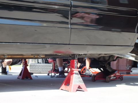 2003 Ford Crown Victoria - Low view beneath a black car on jack stands showing exhaust, legs and tools on the ground.