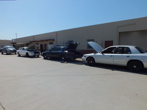2003 Ford Crown Victoria - White, black and silver full-size sedans plus a pickup parked along an industrial building.
