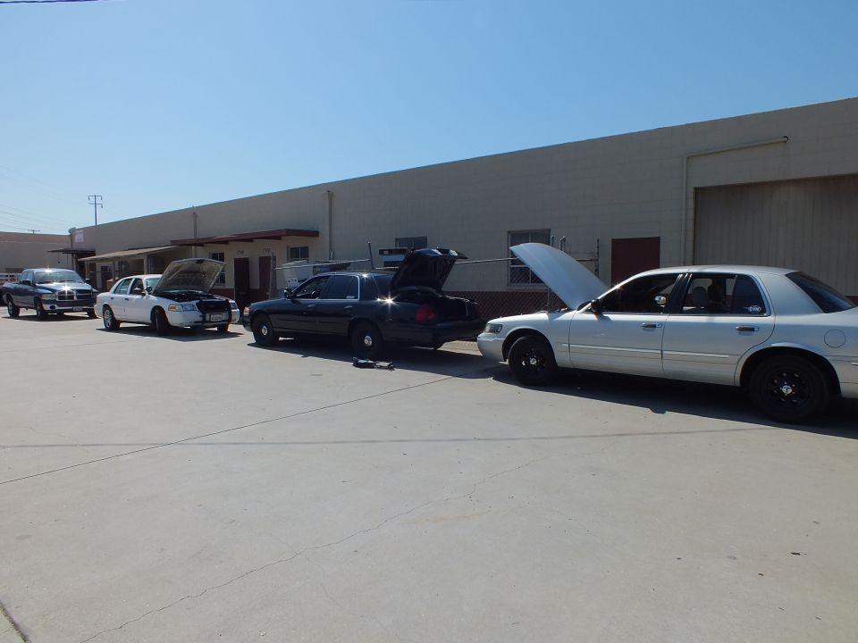 Row of Crown Victoria and Grand Marquis sedans with pickup truck beside warehouse