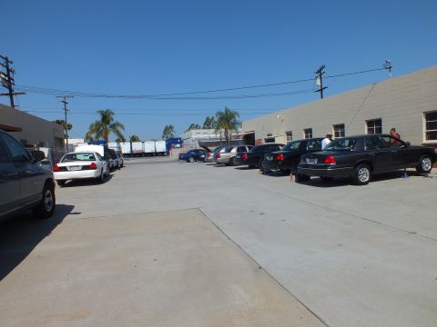 2003 Ford Crown Victoria - Panther-platform sedans and a pickup spread across a large concrete lot beside warehouses.