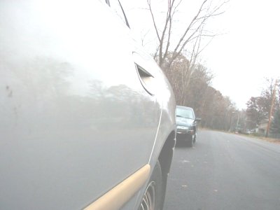 1997 Ford Taurus - A silver car's side is in focus, with another vehicle parked on the side of a road in the background.