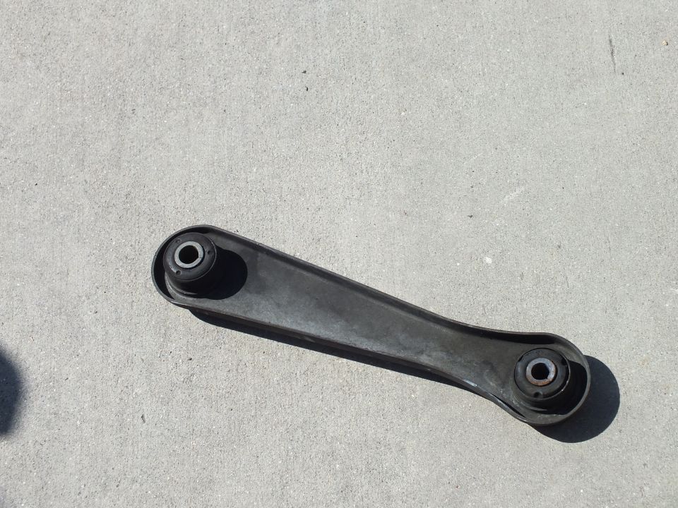Black automotive rear lower control arm with two bushings lying on concrete pavement