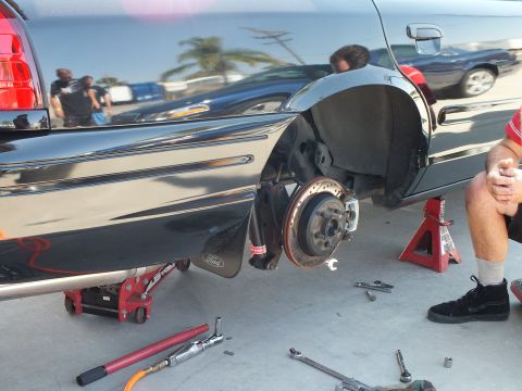 2003 Ford Crown Victoria - Rear quarter of a black Crown Victoria up on stands, wheel removed; floor jack, breaker bar and sockets on the ground.