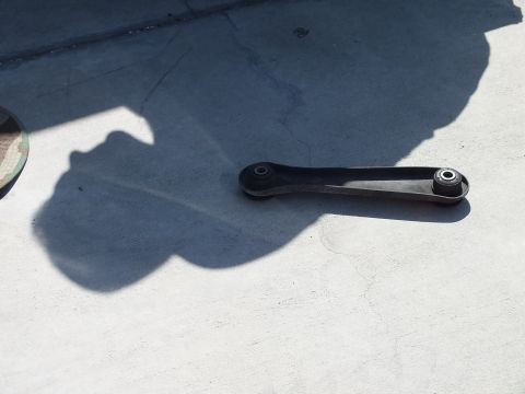 2003 Ford Crown Victoria - removed black control arm lies on stained concrete, the long shadow of the photographer cast across the slab.