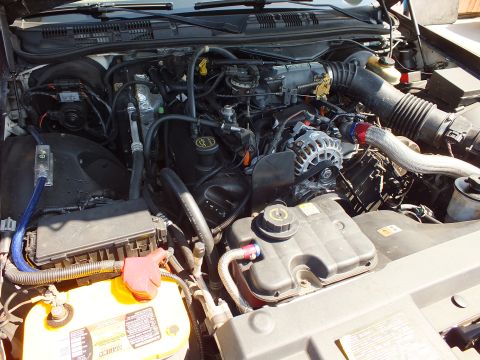 2003 Ford Crown Victoria - Open engine bay of a Ford sedan: SOHC V8 with alternator, coolant reservoir and a yellow-top battery at lower left.