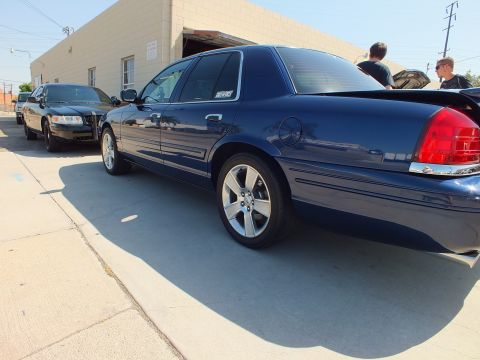 2003 Ford Crown Victoria - Navy Panther-platform sedan shown in profile on alloy wheels in an industrial parking area.
