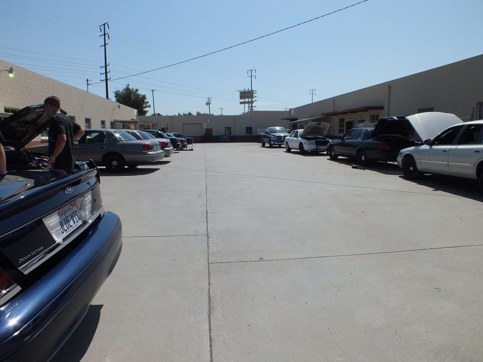 Industrial lot lined with full-size sedans, one with hood up and a California license plate visible