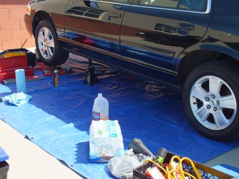 2003 Ford Crown Victoria - Black full-size Ford on jack stands above a tarp, paper towels and a coolant bottle staged for service.