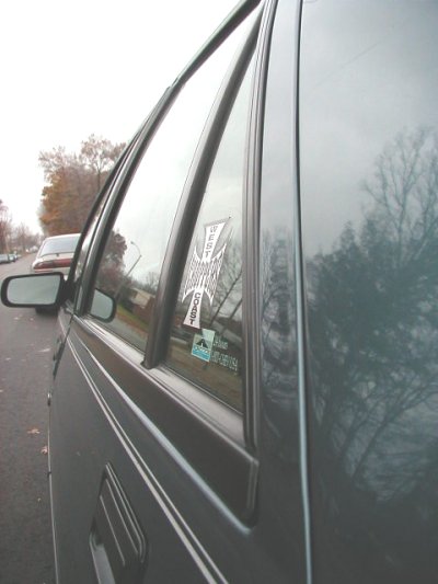 1997 Ford Taurus - Dark sedan's side profile with stickers on the rear window; another vehicle is parked nearby.