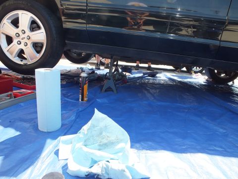 2003 Ford Crown Victoria - Low view under a black Ford showing alloy wheel, jack stand and shop rags on a blue tarp.