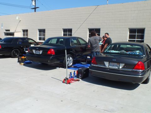 2003 Ford Crown Victoria - Two black Panther sedans parked rear-to-rear with a floor jack and toolbox between them at a shop.