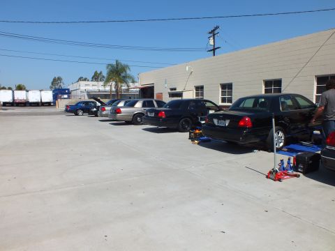 2003 Ford Crown Victoria - Several Panther-platform sedans staged in a row beside a building, nearest car raised on a jack.