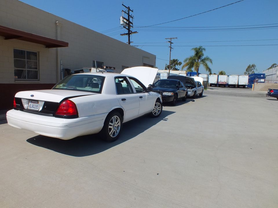 White Ford Crown Victoria with hood up and plate 6LAX285 parked beside other sedans at a shop
