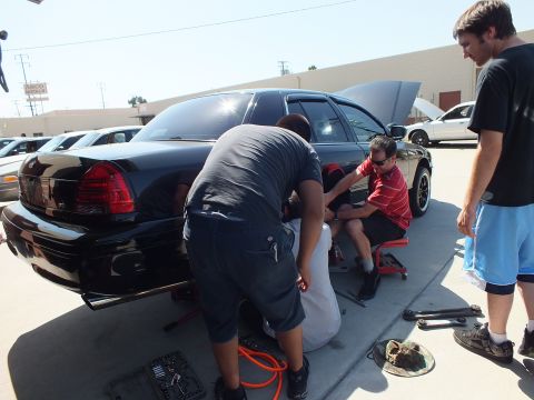 2003 Ford Crown Victoria - Several people kneel around the back of a black full-size Ford, one seated working under the body.