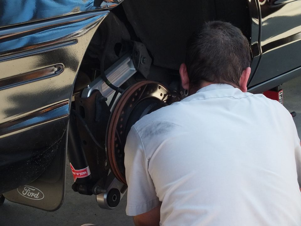 Man in white shirt working on an exposed front brake rotor and caliper of a black Ford with Ford emblem