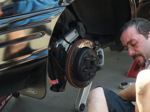 2003 Ford Crown Victoria - Detail of a black Ford front hub and slotted rotor with a tired man resting beside the fender.