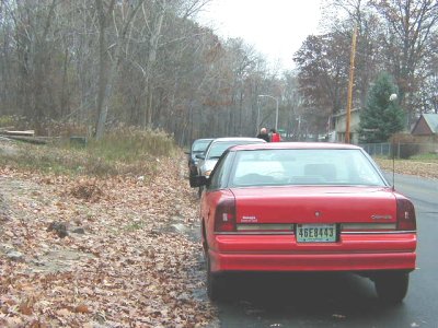 1997 Ford Taurus - A red sedan is parked on the side of a road with fallen leaves and trees in the background.