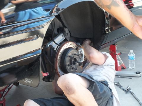 2003 Ford Crown Victoria - Mechanic fits brake pads to a slotted front rotor on a black Ford, wrenches on the pavement.