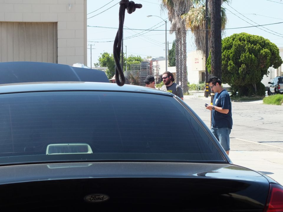 Black Ford with Ford trunk emblem in foreground as men stand talking in an industrial street