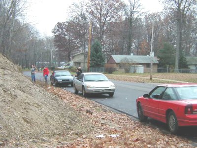1997 Ford Taurus - A silver 1997 Ford Taurus is parked on a residential street alongside other vehicles and individuals.