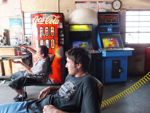 2003 Ford Crown Victoria - Garage hangout scene: Coca-Cola machine, blue arcade game, yellow coiled air hose, wall clock, two seated men
