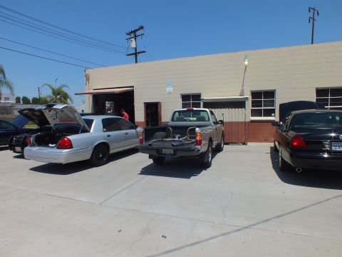 2003 Ford Crown Victoria - Open-trunk silver sedan, a gray pickup, and a black sedan parked outside an industrial garage bay