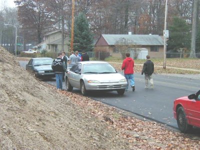 1997 Ford Taurus - Roadside gathering on a leaf-strewn suburban street where a silver Dodge Intrepid sedan is parked at the curb with its hood ajar and a dark…