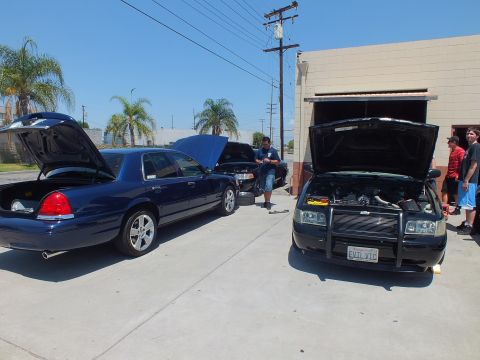 2003 Ford Crown Victoria - Two Panther sedans with open hoods and trunk, one with brush guard reading EVIL VIC, men gathered by the bay