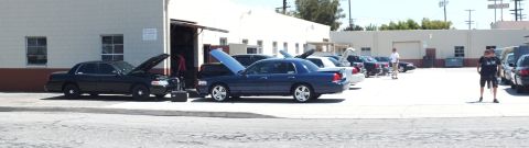 2003 Ford Crown Victoria - Wide panoramic of several Panther sedans parked nose-in at a garage, hoods raised, lone figure at the right