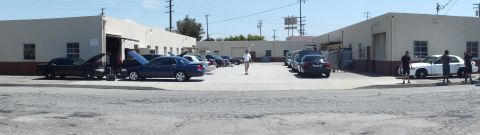 2003 Ford Crown Victoria - Wide shot of a shop yard, dark sedans and a white car parked, several people standing in the open lot