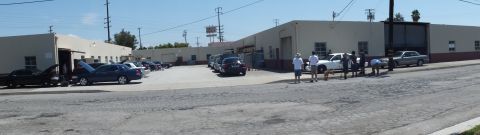 2003 Ford Crown Victoria - Wide view of a garage complex, several dark sedans and a light car parked, people gathered mid-lot
